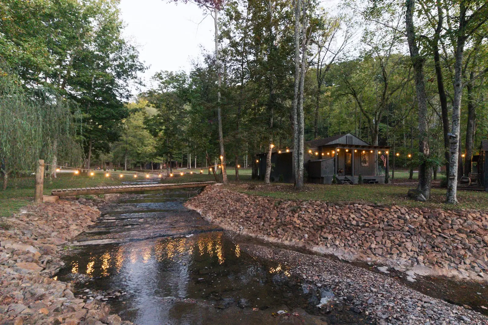 Creek and cabin with string lights at dusk